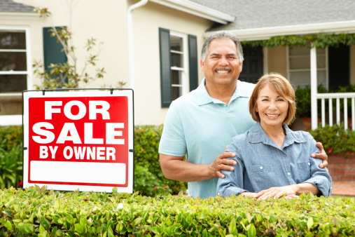 Senior Hispanic couple selling house standing outside home smiling