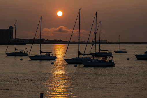 Boston Harbour near Long Wharf in the Financial District in Boston.  This is taken as the sun rises over Logan Airport with yachts moored in the harbour.