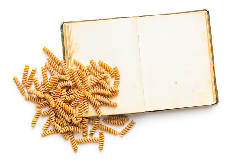 Opend blank recipe book and raw whole grain fusilli pasta isolated on the white background.