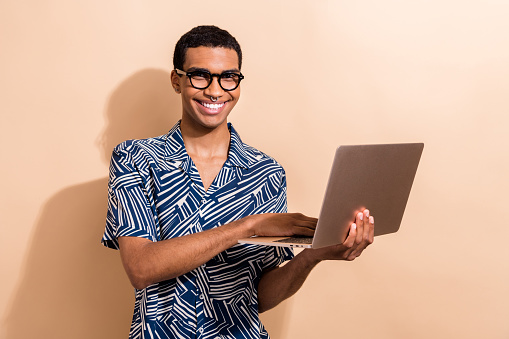 Foto de un hombre exitoso y alegre que usa ropa de moda usa un gadget moderno macbook lenovo aislado sobre fondo de color beige photo