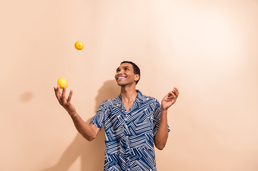 Photo of funny cheerful guy dressed print shirt smiling juggling lemons isolated beige color background.