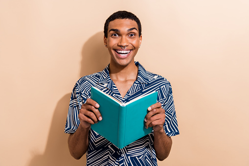 Photo of cheerful excited guy wear print shirt reading interesting book smiling isolated beige color background.