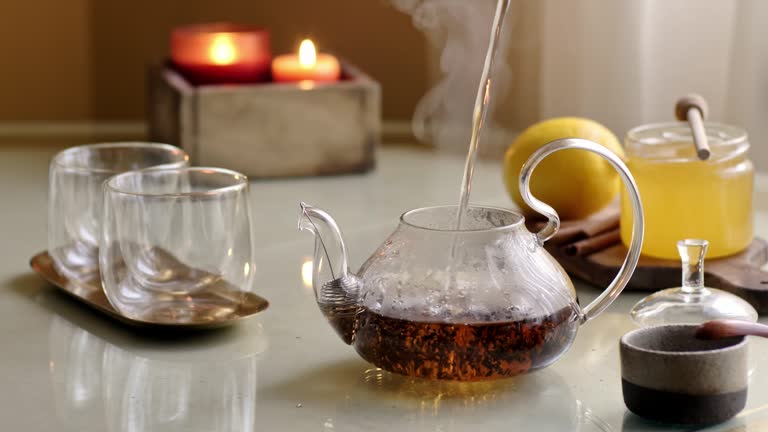 Pour hot steaming water into transparent pot preparing black tea.