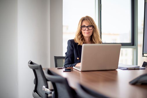 Businesswoman with laptop sitting at desk in a modern office. Confident professional woman working on laptop or having web conference.
