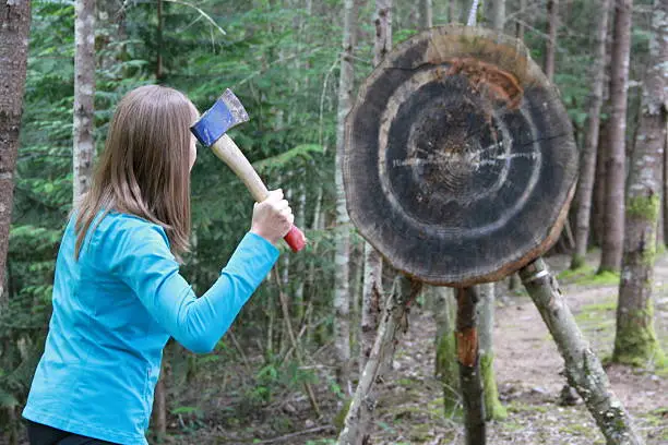 A young woman is preparing to throw a hatchet at a large target in the forest.