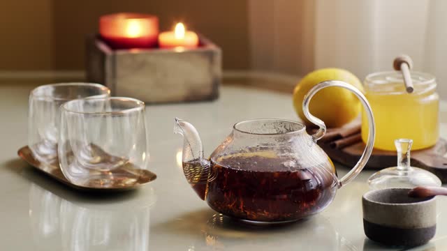 Teapot with hot steamed black tea on table with caps, honey and lemon
