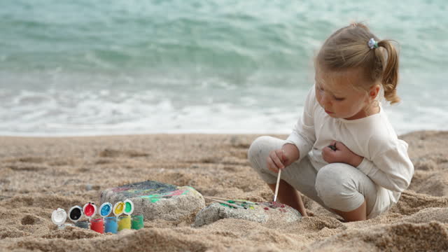 Little girl is painting on sand beach. Play and learn actitvities for vacation