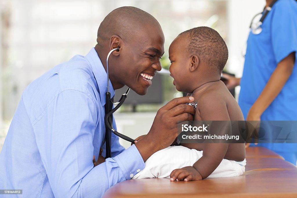 african male doctor examining baby boy happy african male doctor examining baby boy with female nurse on background Doctor Stock Photo