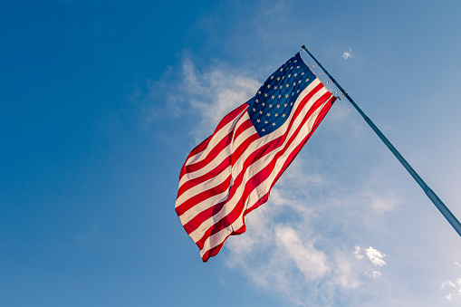 Beautiful American flag waving in the wind, with vibrant red white and blue colors against blue sky, with copy space.