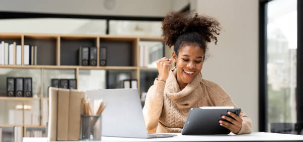 istock Smiling African black business woman using tablet while working on laptop at office. 1781653761