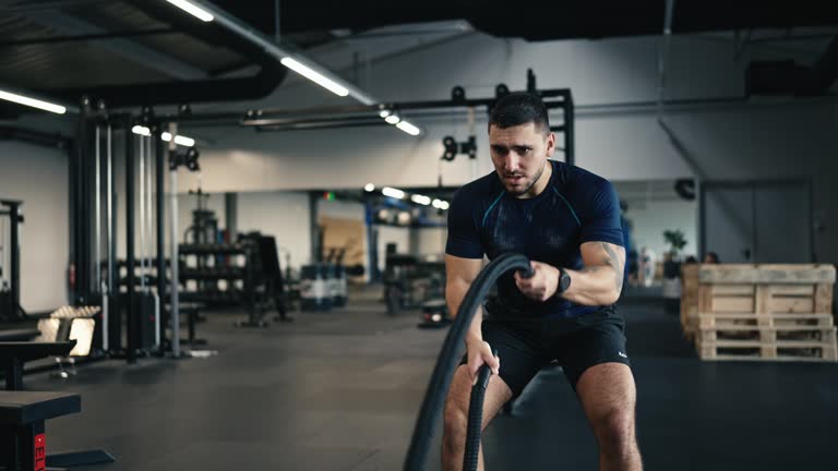 Muscular Man in Sportswear Using Battle Ropes For Strength And Muscle Training in Gym