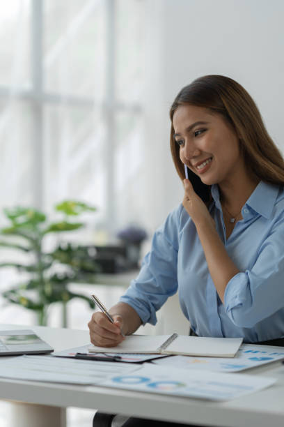 istock Happy Asian businesswoman talking on the phone and smiling while sitting at work using smartphone to talk. Contact via online application, concept of management 1781662664
