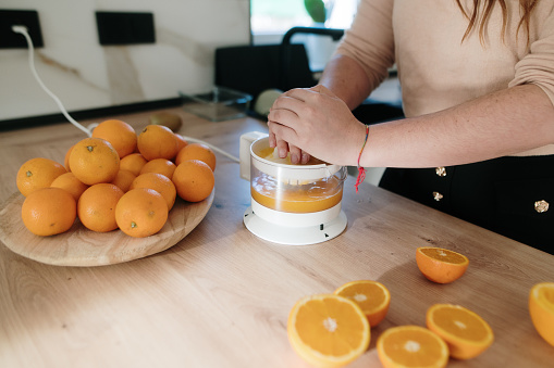 A person in a domestic kitchen using an electric squeezer to make orange juice