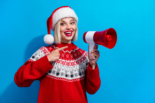 Photo of excited funky lady santa helper dressed ornament sweater showing finger bullhorn empty space isolated blue color background.