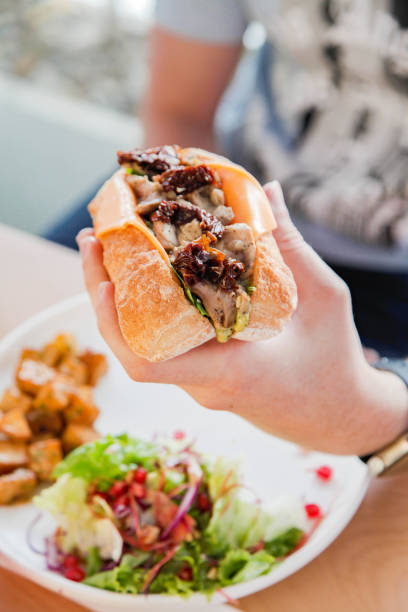 istock Hand holding a Chicken open faced sandwich in ciabatta bread served with veggies on the side. 1781715592