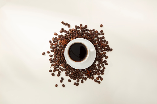 Top view of ceramic cup of coffee placed on brown roasted coffee beans on white background. Clean coffee is an effective active ingredient that helps reduce depression of the nervous system