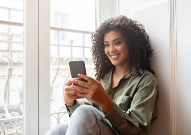 istock African American Lady Texting On Smartphone Sitting On Windowsill Indoor 1781725626