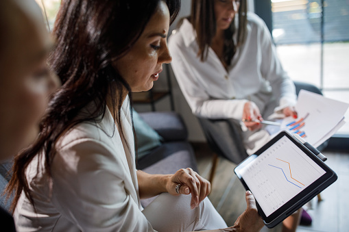 Candid shot of businesswomen sitting in lounge area of the office space and analyzing data for a project that they are co-working on during a meeting.