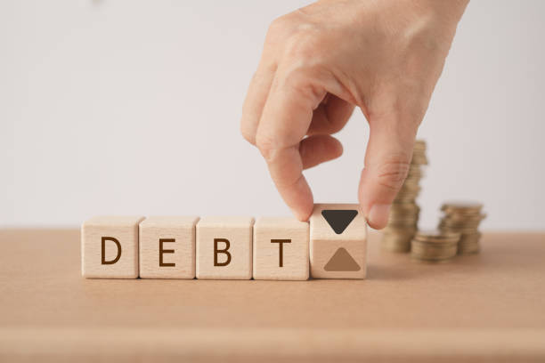 DEBT word on wooden cube blocks word with hand flipped up to down arrow and blurred stack of coin  for Financial debt decrease, revenue management  concept