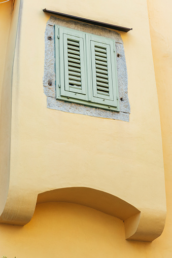 Bay window with a window closed with green wooden shutters on a yellow wall