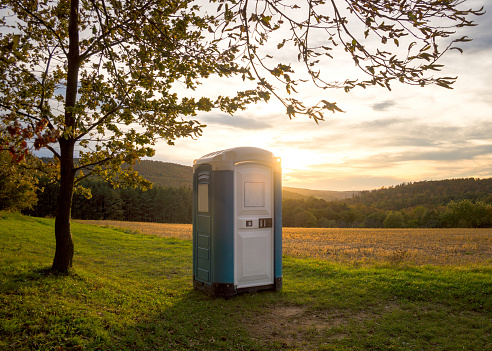 blue plastic toilet cabin in woodland at sunset