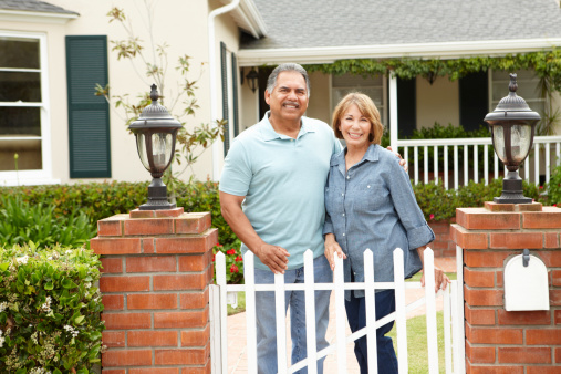 Senior Hispanic couple outside home standing still smiling at camera