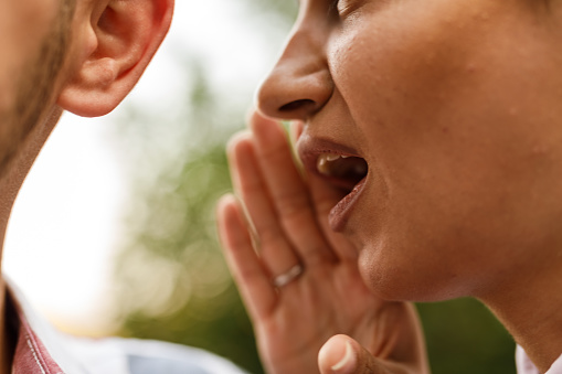 Close up shot of young woman whispering a secret into friends' ear when hanging out.