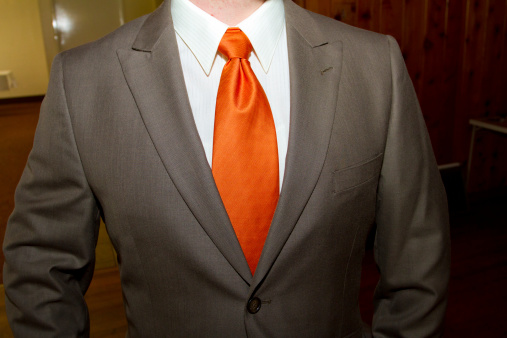 A groom wears a brown suit and an orange tie on his wedding day.