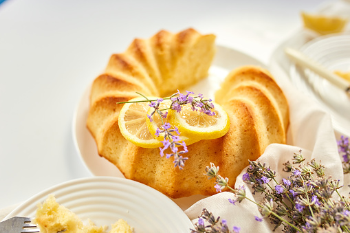 Piece of lemon cake on white table with lavender flower bouquet