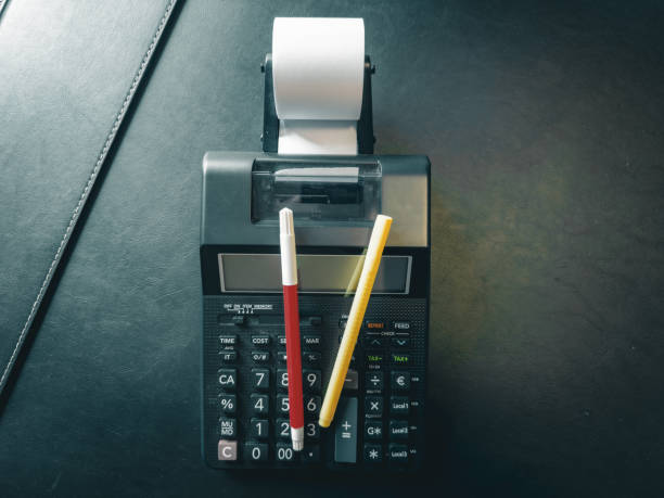 A printing calculator isolated on a black background on top of a desk.