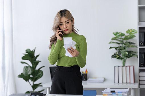Asian businesswoman using mobile phone to make contact Inquire about expenses on bills, debt obligations, insurance or loans. Real estate consultants about offering mortgage loans in a home office.