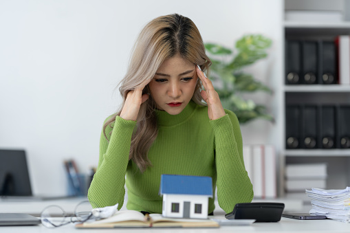 Asian businesswoman suffering from stress, fatigue, headache from working with bills, debts, insurance or loans. Real Estate Home Residential Consult about mortgage loan offerings in the office.