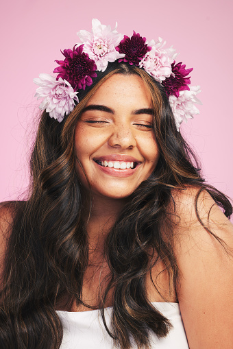 Woman, flowers and smile with crown on pink background for natural beauty, skincare and self care in studio. Face, happy model and floral hair band for sustainability, eco dermatology and cosmetics
