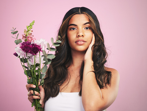 Woman, flowers and portrait in studio for skincare, cosmetics and natural aesthetic on pink background. Face, model and eco beauty with floral plants, sustainability and bouquet for vegan dermatology