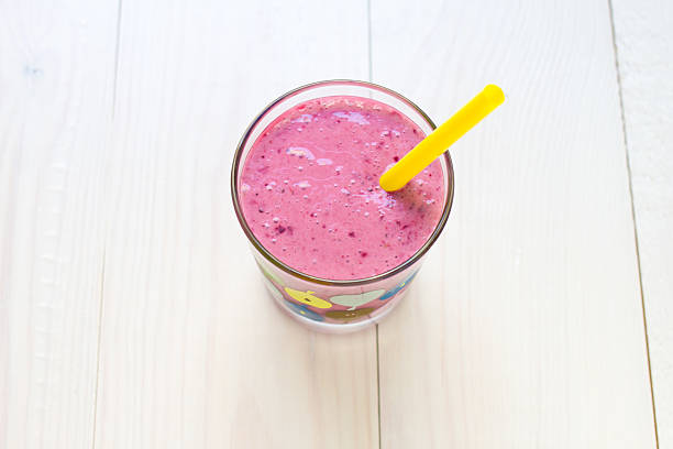 Strawberry smoothie with a straw, close up, on white wooden background