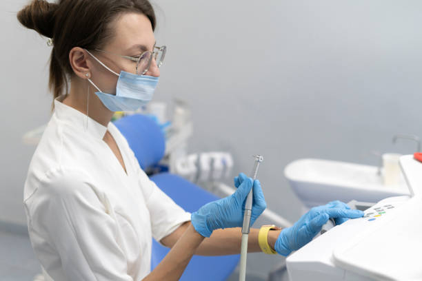 dentiste en gants bleus prenant la perceuse d’un tableau de bord de machine dentaire pour traiter un patient dans une clinique - dental hygiene dental equipment dental drill practicing photos et images de collection