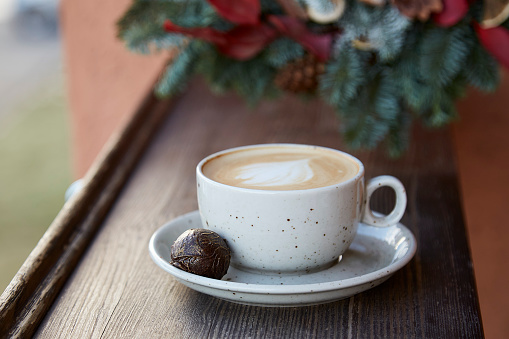 Coffee cup outdoor at cozy terrace near Christmas wreath. Aesthetic cozy home.