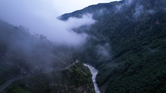 A beautiful view of a lush green mountain valley with a large river and road during a misty day