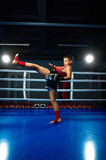 full length portrait of little athletic boy, professional martial arts sportsman training on ring before fight at the sport club. Concept of sport, healthy lifestyle, hobby, workout, competition.