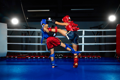 Children, martial fighter exercising kickboxing with sparring partner, fighting in ring at gym. Young professional sportsmen. Concept of sport, healthy lifestyle, hobby, fitness workout, competition.