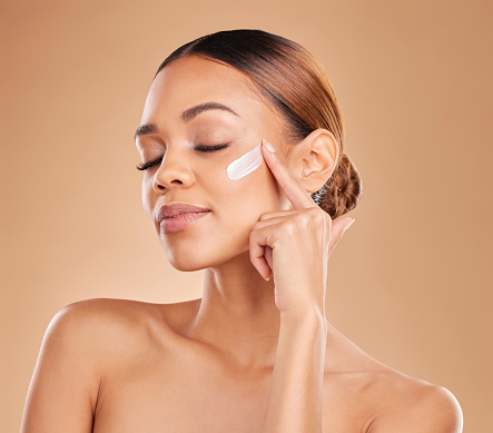 Face, beauty skincare and woman with cream in studio isolated on a brown background. Dermatology, cosmetics and mixed race female model with lotion, creme or facial moisturizer product of skin health