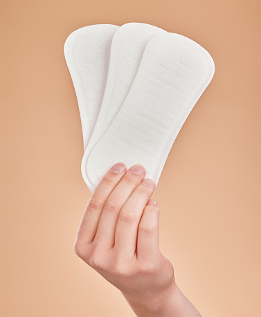 Hand, sanitary pads and period with a woman in studio on a brown background for female hygiene or care. Lifestyle, and gynecology with a female holding a feminine product for her menstrual cycle