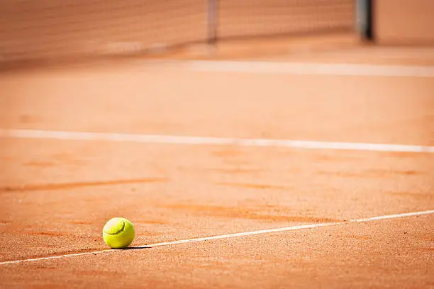 yellow tennis ball on orange sand and white lines