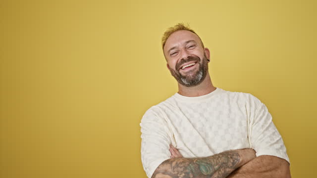 Attractive young man, standing with a confident smile and casual arms crossed gesture. isolated on a yellow background, exuding sheer happiness and positive joy.