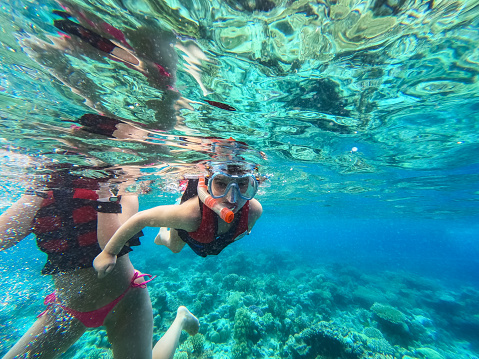 Cute little girl snorkeling in the Red sea in Hurghada in Egypt with her mother next to her.
