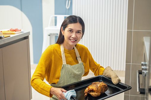 Female holding the roasted chicken which she prepared for meal for thanksgiving dinner party