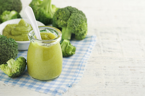 Green broccoli baby food in white bowl and jar on table. Green baby food. Child first feeding concept. Baby Natural Food. Production and menu of baby food. Selective focus.
