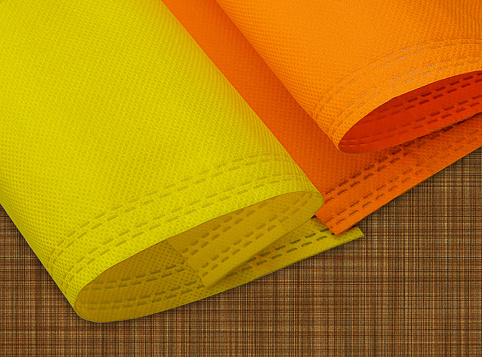 two rolls of yellow and orange colored non-woven fabric on a fibrous brown surface. polypropylene fabric