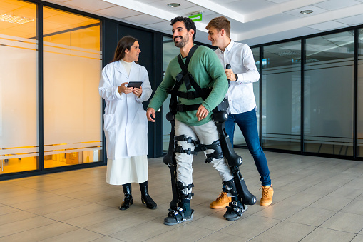 Mechanical exoskeleton, female doctor with device walking with disabled person with robotic skeleton in rehabilitation, physiotherapy in modern hospital, futuristic physiotherapy