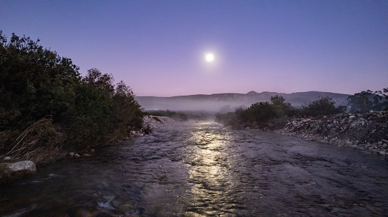 Full moon icy cold morning dawn over flowing river and rural mist
